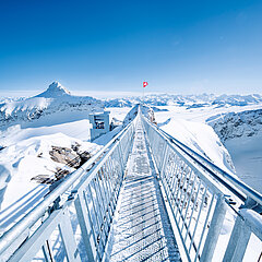 Die Hängebrücke «Peak Walk» auf dem Glacier 3000 vor verschneiter Bergkulisse und Bergrestaurant Botta.