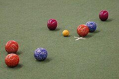 Viele farbige Bälle in verschiedenen Grössen liegen auf grünem Boden.