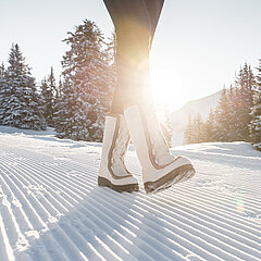  Jambes de femme, chaussées de raquettes blanches, marchant sur un sentier de randonnée d’hiver fraîchement damé.