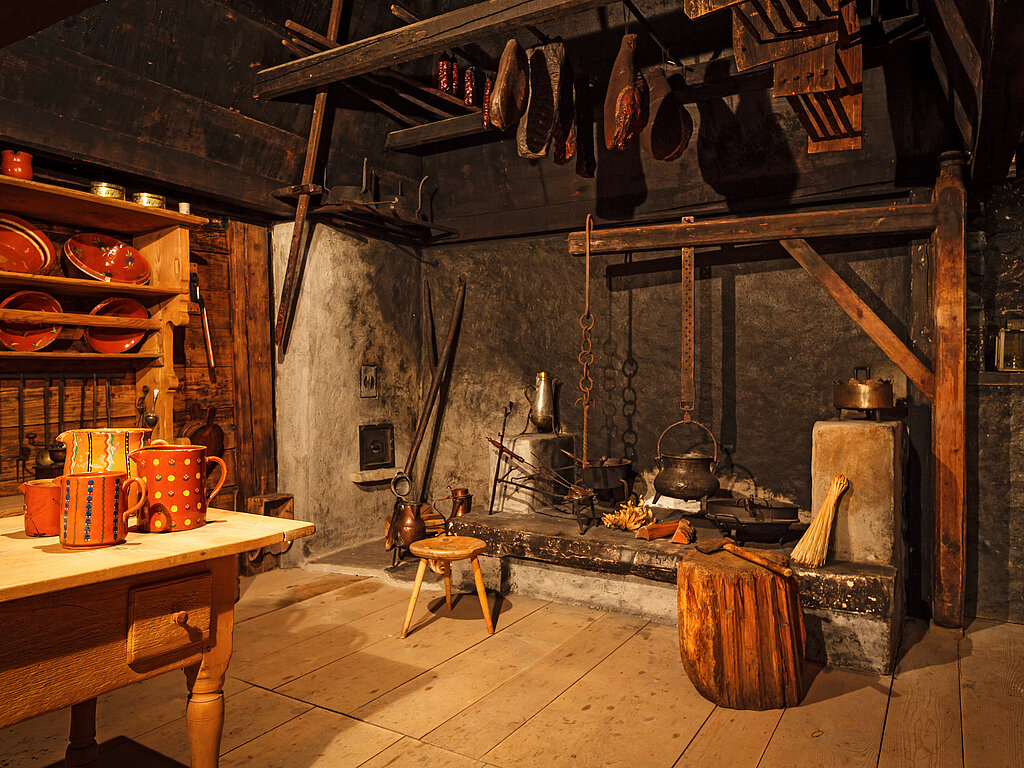 <p>Alte Küche mit einem Kamin und einem hölzernen Tisch im Landschaftsmuseum in Saanen.</p>