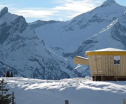Hölzernes XXL Fondue Caquelon vor verschneitem Bergpanorama.