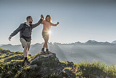 Eine Frau balanciert über einen grossen Stein und ein Mann stützt sie mit der Hand.