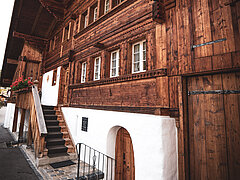 Historisches Holzhaus in Zweisimmen mit dunkelbrauner Fassade, geschnitzten Balken, Holzfenstern und Treppe zum erhöhten Eingang.