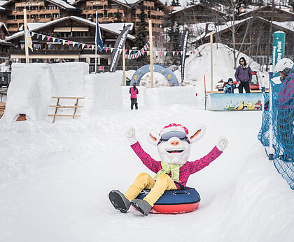Saani, das Saanenland-Maskottchen rutscht auf einem Ring auf der Piste im Winterspielplatz Saanenmöser.