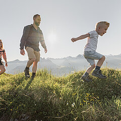 Famille composée de trois personnes se promenant dans de vertes prairies par un temps estival.