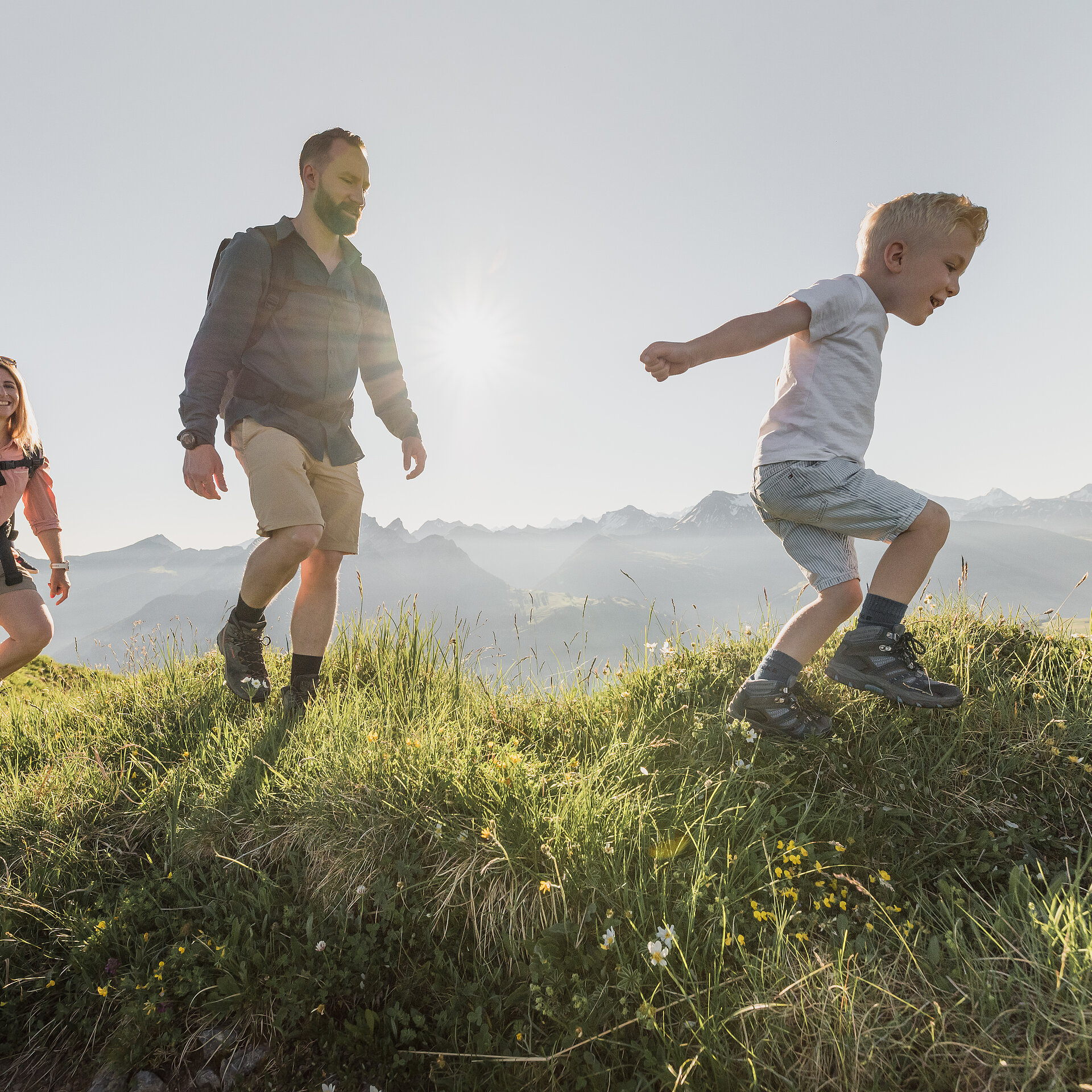 <p>Familie bestehend aus drei Personen beim Wandern über grüne Wiesen bei sommerlichem Wetter.</p>