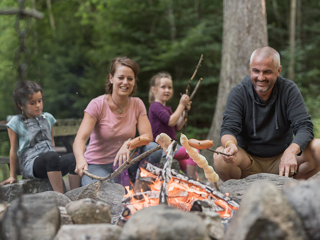 <p>Familie mit zwei Kinder grilliert am Feuer Cervelats und Schlangenbrot.</p>