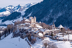 Verschneites Schloss Greyerz über dem mittelalterlichen Städtchen Greyerz, umgeben von Winterlandschaft und Bergen.