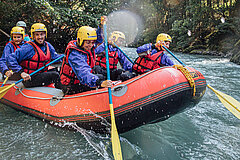 Un groupe de personnes est assis dans un bateau en caoutchouc rouge avec des rames jaunes sur des eaux sauvages.