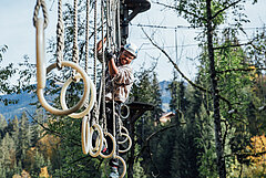Ein Kind mit Kletterausrüstung klettert über einen Parcours im Seilpark.