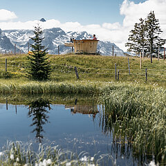 A small mountain lake with a giant fondue caquelon and spectacular scenery beyond.