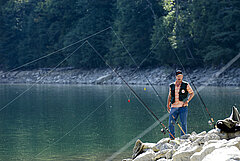 Ein Mann, bekleidet mit einem orangenfarbenen T-Shirt steht am Ufer des Arnensees und kontrolliert seine fixierten Angelruten