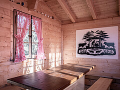 Small wooden chalet from the inside with table and benches.