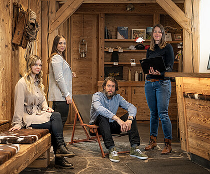 In einem urchigen Empfangsbüro erwarten drei Frauen und ein Mann gespannt ihre Gäste.