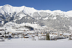 Verschneites Dorf Frutigen im Talboden, umgeben von weiten Schneefeldern und imposanten Berggipfeln im Hintergrund.
