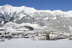 Village de Frutigen enneigé au fond de la vallée, entouré de vastes champs de neige et de sommets montagneux en arrière‑plan.