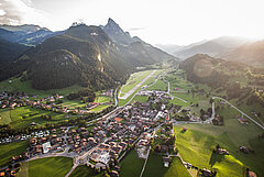 Sommer-Luftaufnahme vom Dorf Saanen und dem Flugplatz mit dem Le Rubli Gipfel und weiteren Bergen im Hintergrund.
