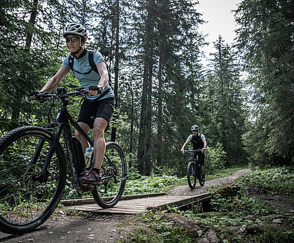 Ein älteres Mountainbike Pärchen fahren auf dem Turbach Trail gerade über eine Brücke. Der Trail liegt im Wald.