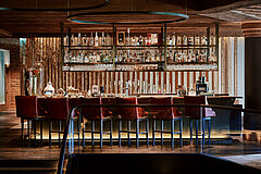 Elegant lounge bar with a lit counter, bar stools and a large shelf displaying spirits and glassware.