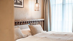 Chambre de l'hôtel The Mansard à Gstaad aux tons chaleureux de beige et de gris. La pièce est lumineuse et une voile légère et transparente habille la fenêtre.