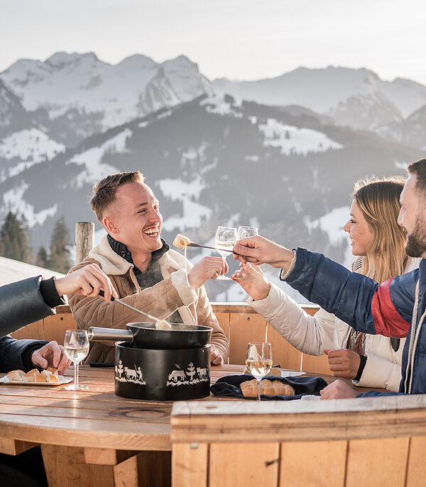 <p>Eine Gruppe von Freunden beim Fondue essen im Fondue Caquelon bei winterlicher Stimmung.</p>