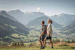 Ein Paar wandert auf einem Berg, im Hintergrund das Saanenland mit Bergkulisse.