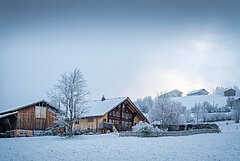 Bauernhaus und Scheune mit Garten in winterlicher Landschaft.