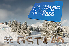 Winter landscape with snow-covered trees, ski slope and Magic Pass display against a clear blue sky.