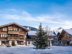 Dorfplatz in Saanen im Winter mit einer grünen Tanne in der Mitte. Rundum typische hölzerne Chalets.