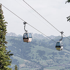 Two gondolas going up a mountain, with a mountain panorama behind them.