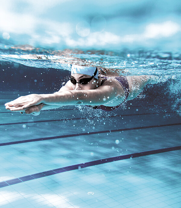Eine Schwimmerin mit Schwimmmütze und Brille taucht in einem Hallenbad.
