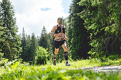 Ein Trailrunner der auf einem Kiesweg durch eine Lichtung im Wald rennt. Das Bild ist von unten aufgenommen.