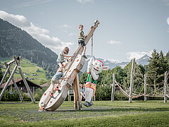 Eine Kletterwand in Form einer Geige, auf welcher drei Kinder und Saani spielen.