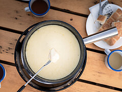 Sicht von oben auf einen Tisch mit schwarzem Fonduecaquelon und Brot.