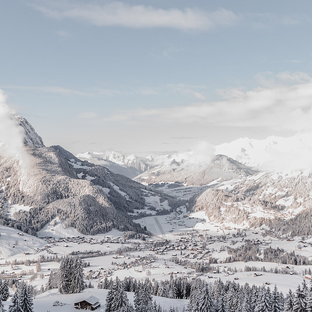 <p>Panoramablick auf das winterliche Dorf Saanen mit dem Flugplatz und Bergen im Hintergrund.</p>