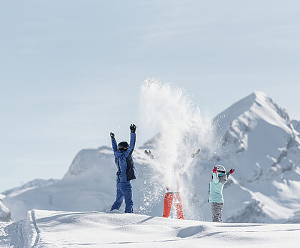 Zwei Kinder und ein Erwachsener werfen Pulverschnee in die Höhe