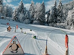 Parc d’apprentissage avec figures colorées et modules d’exercices sur neige fraîche, entouré d’arbres enneigés.