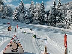 Learning park with colorful figures and training elements on groomed snow, surrounded by snow-covered trees.
