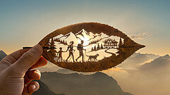 Artistically cut leaf showing hikers, a dog, a chalet and mountain scenery at sunrise in the holiday region Gstaad.