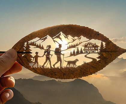 Künstlerisch ausgeschnittenes Blatt mit Wandernden, Hund, Chalet und Berglandschaft vor Sonnenaufgang in der Ferienregion Gstaad.