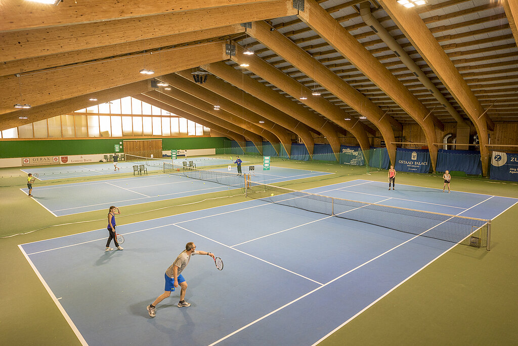 <p>Eine Gruppe von Menschen spielen in einer grossen hölzernen Halle Tennis.</p>