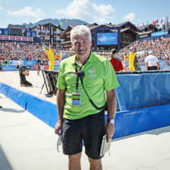 Tournament director Ruedi Kunz in front of the beach volleyball court, with many spectators in the stands in the background.