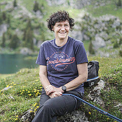 Dame vêtue d'un T-shirt foncé imprimé, assise sur une pierre près du Seebergsee.